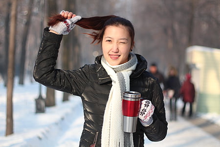 woman holding her hair and grey mug standing on snow covered ground thumbnail