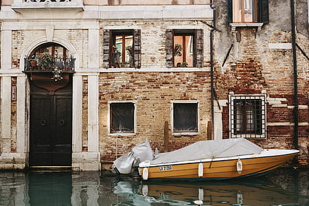 brown and white speedboat on body of water next to concrete building thumbnail