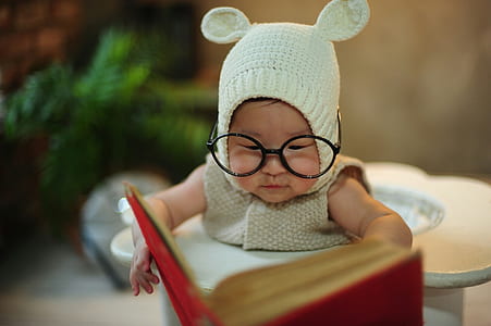 baby wearing gray knitted pram suit and eyeglasses holding book thumbnail