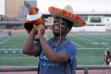selective focus photography of man holding brown and white cap beside football stadium during daytime thumbnail