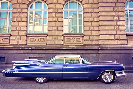 classic blue coupe parked near brown building thumbnail