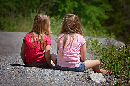 two girls sitting on concrete road during day thumbnail