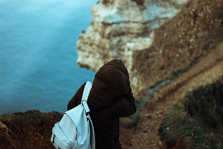 person in black hoodie with backpack walking in pathway near body of water during daytime thumbnail