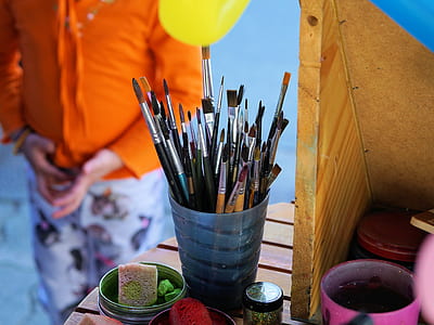 assorted-color paint brush in blue plastic container on brown wooden surface thumbnail