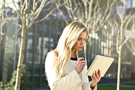 Young Woman In White Jacket Using Smartphone And Tablet While Walking on the Road thumbnail