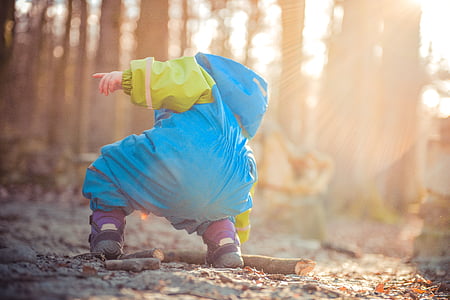 toddler in raincoat holding brown wood near trees thumbnail