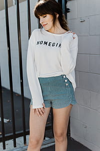 woman wearing long-sleeved shirt and striped short shorts standing outside metal gate thumbnail