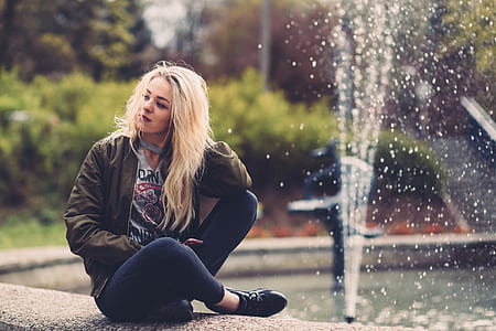 woman in green jacket sitting beside water fountain thumbnail