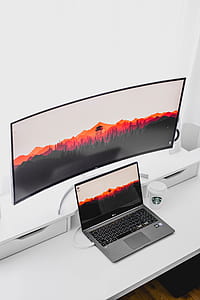 curved monitor, laptop computer, and Starbucks cup on white wooden table thumbnail