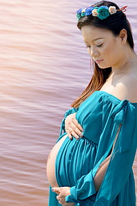 woman taking photo while holding her tummy near body of water thumbnail