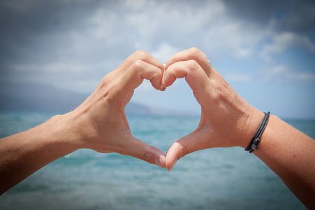person making heart hand sign in front of sea thumbnail