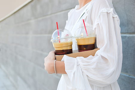 woman wearing white crew-neck long-sleeved dress holding two disposable solo cups with red straws at daytime thumbnail