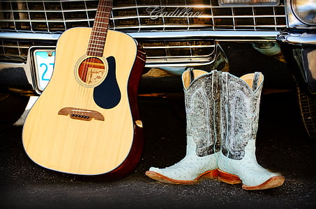 brown dreadnought acoustic guitar beside pair of cowboy boots thumbnail