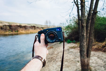 person holding black camera near river thumbnail