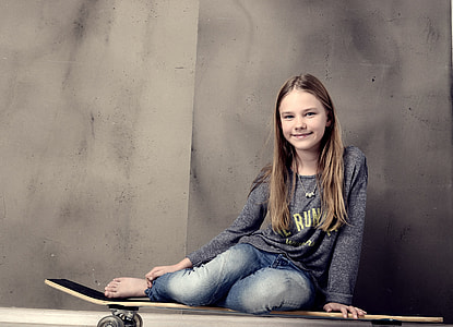 smiling woman sitting on skateboard near wall thumbnail