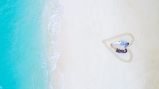 Man and Woman Lying on White Sand Near Sea Shore thumbnail