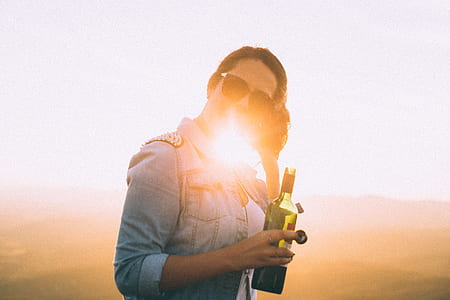 Woman Wearing Blue Denim Jacket Holding Wine Bottle in Golden Hour Photo thumbnail