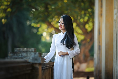 woman wearing white long-sleeved shirt standing holding the brown wooden rail during daytime thumbnail