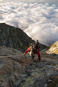 man climbing on gray rock formation near white clouds and blue sky thumbnail