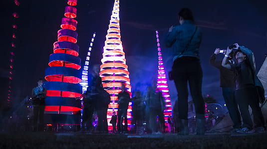low angle photography of group of people standing beside lighted tower while holding smartphone thumbnail