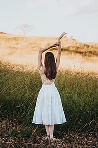woman wearing white dress raising her two hands near green grass field during daytime thumbnail