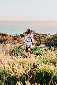 woman in pink bomber jacket standing above green grass holding head near body of water thumbnail