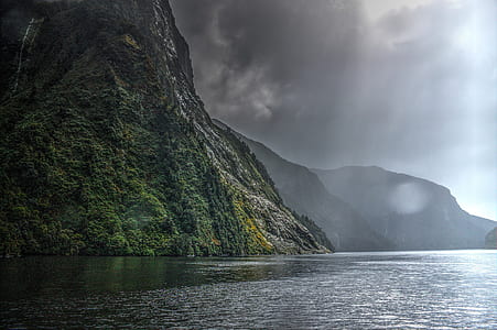 landscape photography of black and green mountain range beside body of water thumbnail