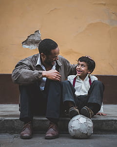 man and boy standing beside each other on sidewalk while talking and laughing together thumbnail