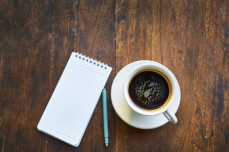 cup of coffee on saucer beside notebook and pen thumbnail
