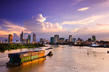 cargo vessel with intermodal containers on body of water near high-rise buildings thumbnail