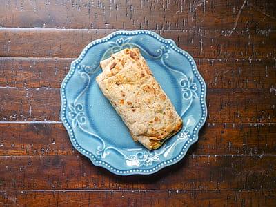 Top view of spinach, feta cheese, and egg all wrapped in a tortilla. Sitting on a blue plate in the sunlight. thumbnail