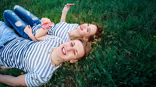 couple wearing gray-and-white striped shirts lying on green grass at daytime thumbnail