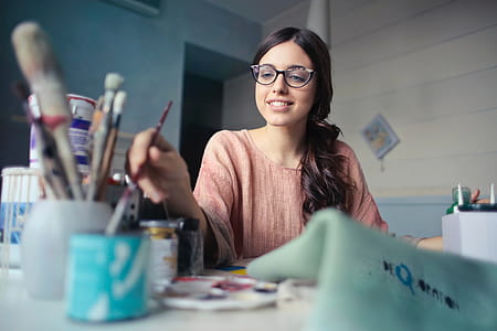 A young woman with glasses painting with a brush in her hand thumbnail