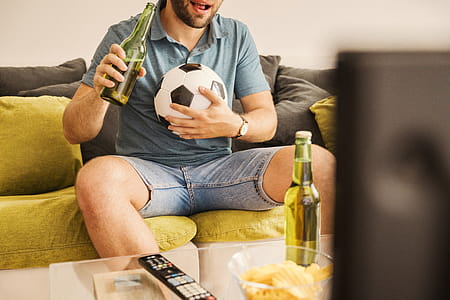 Young man watching football on TV and drinking beer at home thumbnail
