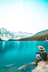 person sitting on rugged cliff overlooking teal calm body of water at daytime thumbnail
