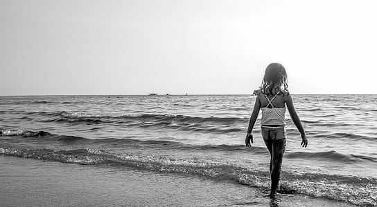 Grayscale Photo of Girl Walking on Seashore With White Spaghetti Strap Top thumbnail