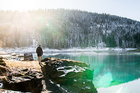 person standing on rock formation near lake surround by mountains thumbnail