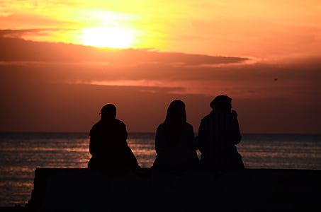 silhouette of three people sitting near body of water during golden hour thumbnail