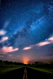 asphalt road between green grass during nighttime thumbnail