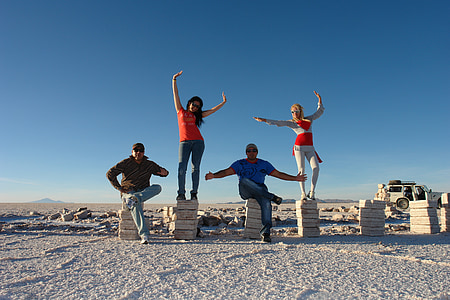 four people posing on pedestals in desert under clear day sky thumbnail