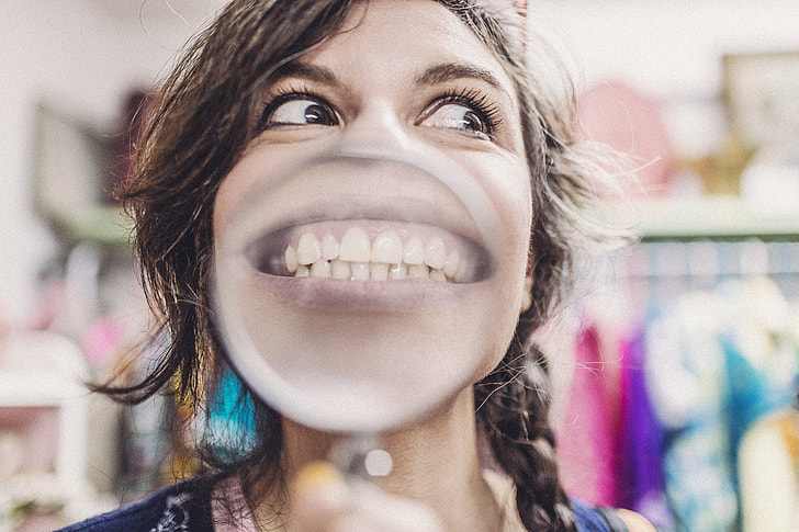 Woman  Showing Teeth while holding Magnifying Glass