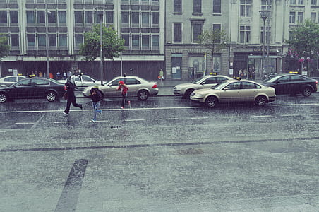 three people running on concrete road beside vehicles and building while raining thumbnail
