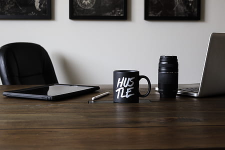 black hustle-printed ceramic mug beside black camera lens and white Apple Pencil thumbnail