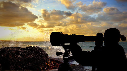 silhouette of person using telescope beside ocean during golden hour thumbnail