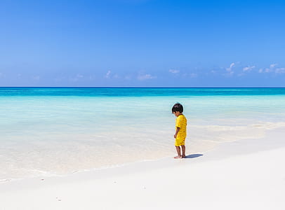 boy wearing yellow top and shorts standing on white sand during daytime thumbnail