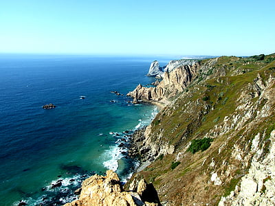 green rock formation beside calm water thumbnail