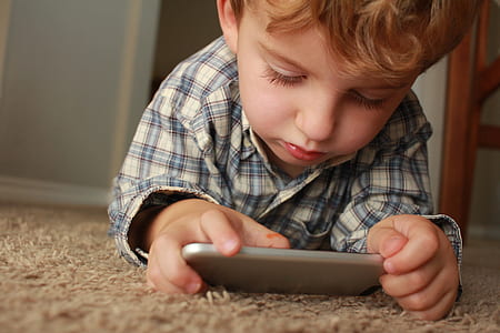boy lying on brown carpet looking at smartphone thumbnail