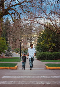 man walking holding hands with boy under leafless tree thumbnail