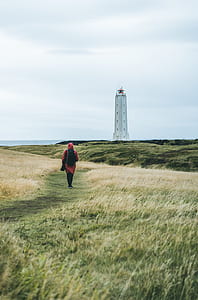 woman walking near white concrete building under white clouds during daytime thumbnail
