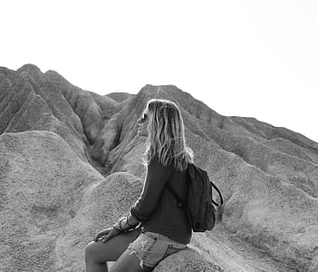 grayscale photography of woman sitting on rock formation thumbnail